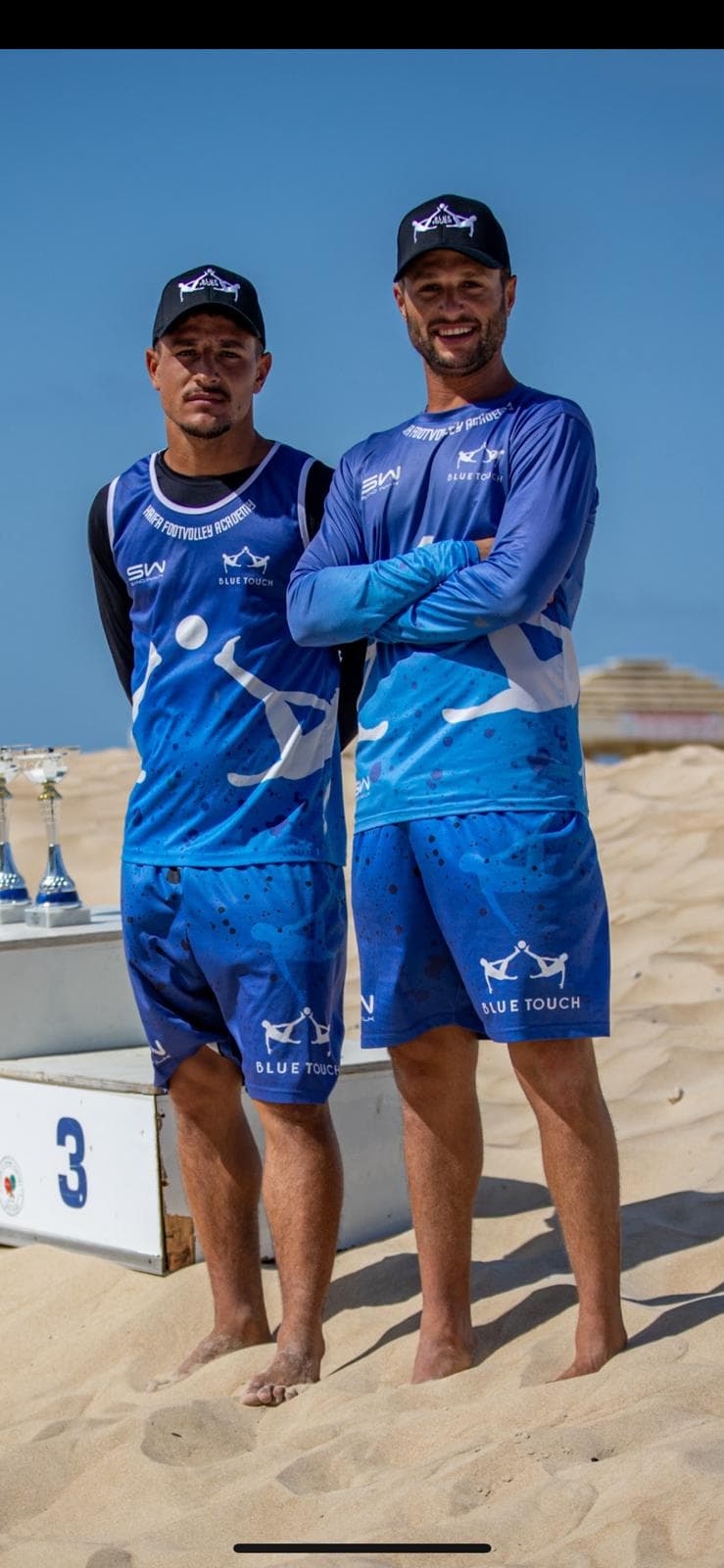 יוסי וענבר, מייסדי בלו טאצ', עומדים יחד על החול עם כובעי המועדון